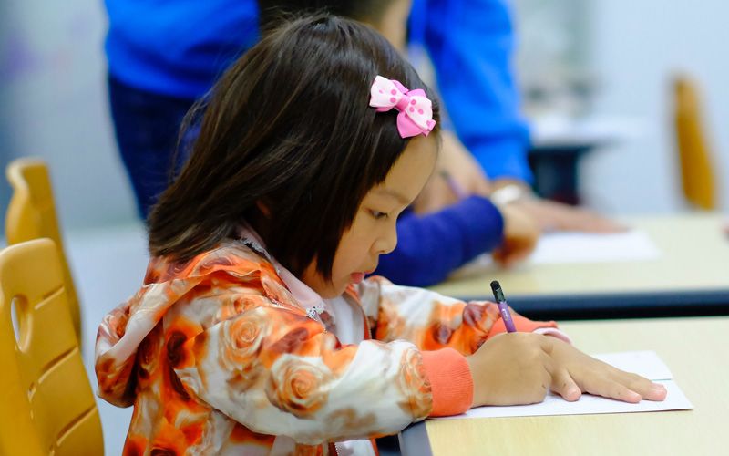 photo d'une enfant assise à un bureau d'école et qui écrit sur une feuille